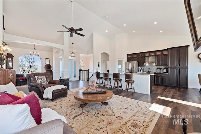 living room with dark wood-type flooring, high vaulted ceiling, ceiling fan with notable chandelier, recessed lighting, and arched walkways