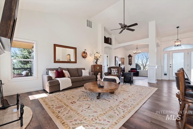 living area with visible vents, dark wood-type flooring, high vaulted ceiling, ceiling fan with notable chandelier, and arched walkways