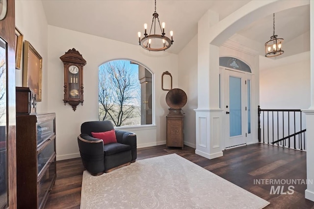 living area featuring baseboards, dark wood finished floors, vaulted ceiling, arched walkways, and a notable chandelier