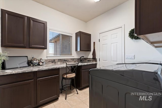 kitchen featuring washer and dryer, dark brown cabinetry, light tile patterned flooring, and a sink