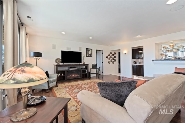 living room with a glass covered fireplace, wood finished floors, recessed lighting, and visible vents