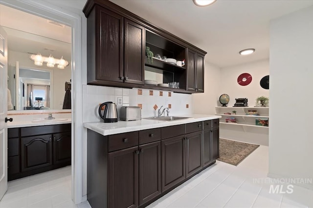 kitchen featuring a sink, open shelves, backsplash, dark brown cabinetry, and light countertops