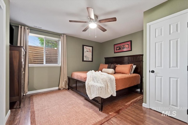 bedroom featuring ceiling fan, visible vents, baseboards, and wood finished floors