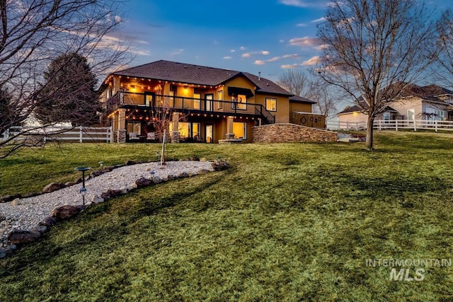 back of house at dusk featuring stucco siding, a yard, fence, and a wooden deck