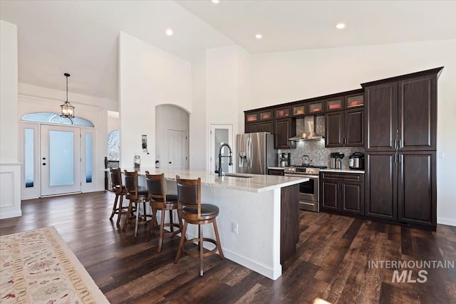 kitchen featuring a kitchen island with sink, a kitchen bar, appliances with stainless steel finishes, wall chimney exhaust hood, and a sink