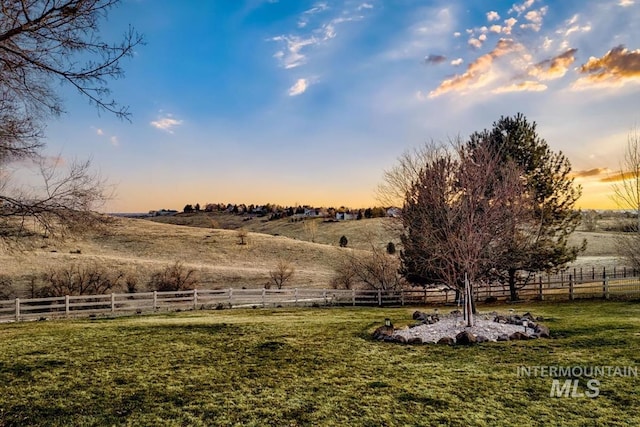 yard at dusk featuring a rural view and fence