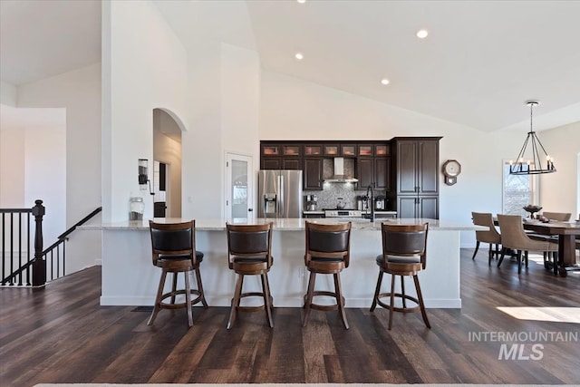 kitchen featuring backsplash, glass insert cabinets, dark wood finished floors, stainless steel refrigerator with ice dispenser, and wall chimney exhaust hood