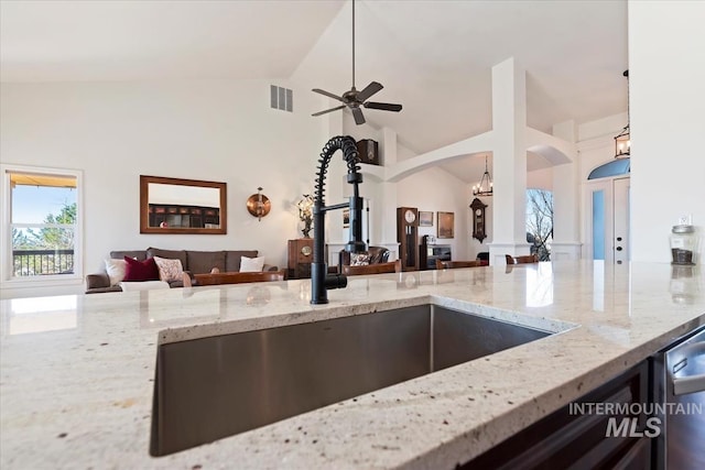 kitchen with visible vents, a sink, light stone counters, open floor plan, and arched walkways