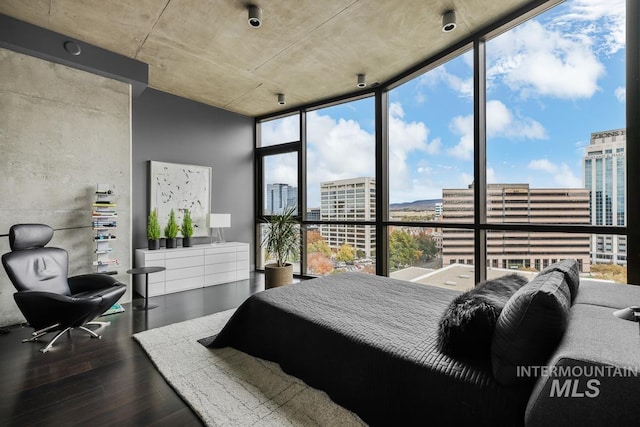 bedroom with wood finished floors, a wall of windows, and a view of city