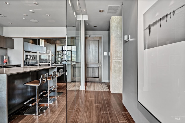 kitchen featuring modern cabinets, stainless steel oven, dark wood finished floors, a kitchen bar, and recessed lighting