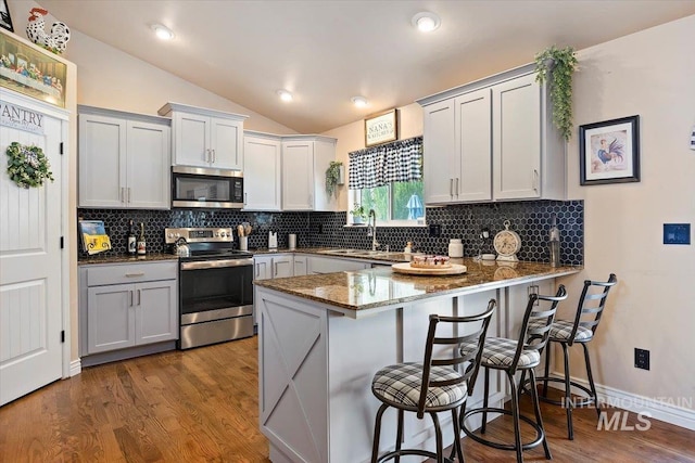 kitchen with sink, lofted ceiling, kitchen peninsula, a breakfast bar area, and appliances with stainless steel finishes