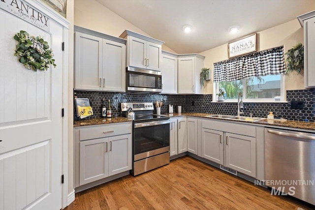 kitchen with stainless steel appliances, sink, lofted ceiling, light wood-type flooring, and gray cabinets