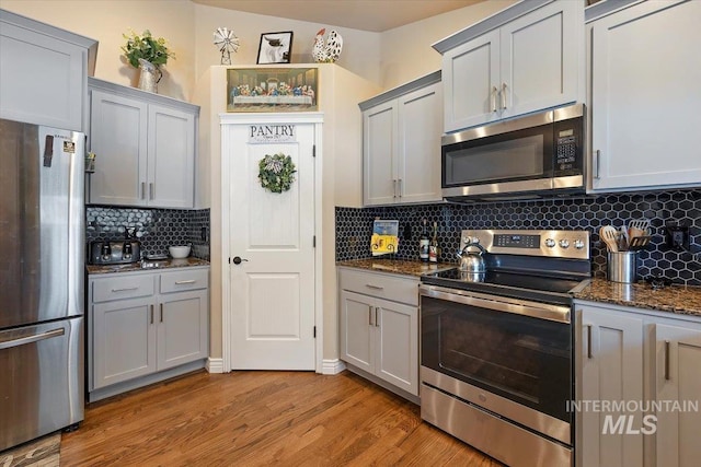 kitchen featuring gray cabinetry, stainless steel appliances, dark stone counters, decorative backsplash, and light hardwood / wood-style flooring