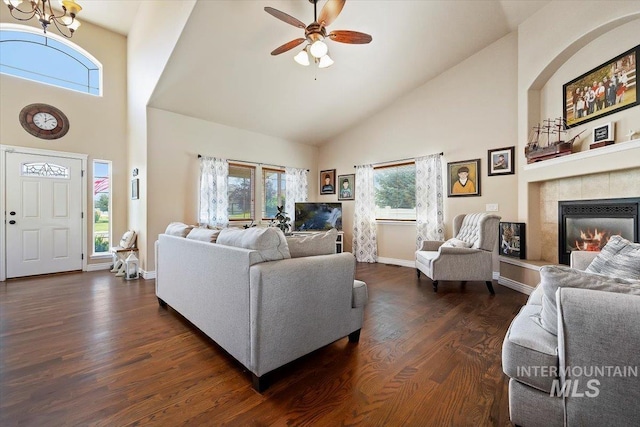 living room featuring ceiling fan with notable chandelier, dark hardwood / wood-style flooring, a tiled fireplace, and a healthy amount of sunlight