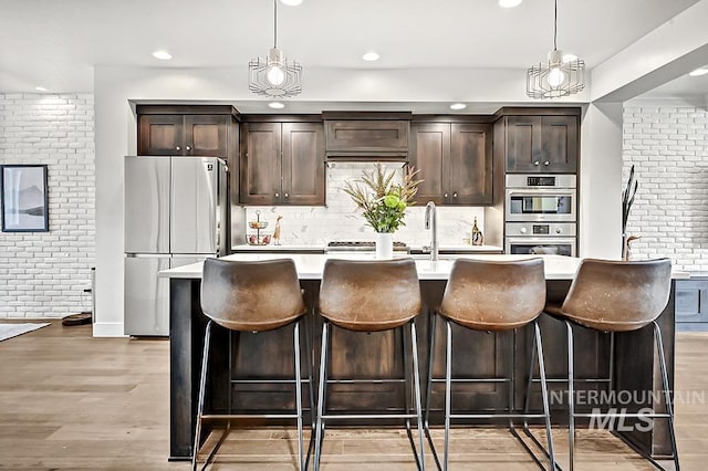 kitchen featuring freestanding refrigerator, dark brown cabinets, stainless steel double oven, and a kitchen island with sink