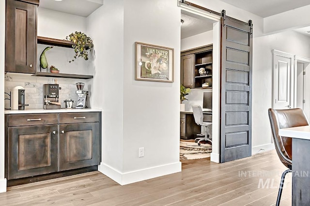 interior space with a barn door, baseboards, decorative backsplash, and light wood-style flooring
