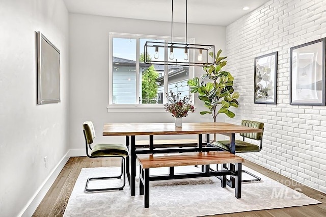 dining area featuring baseboards, brick wall, and wood finished floors