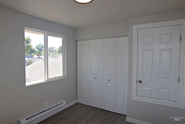 unfurnished bedroom featuring baseboard heating, dark hardwood / wood-style floors, and a closet