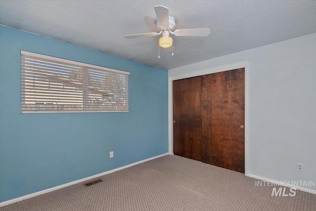 unfurnished bedroom with carpet flooring, ceiling fan, a closet, and a textured ceiling