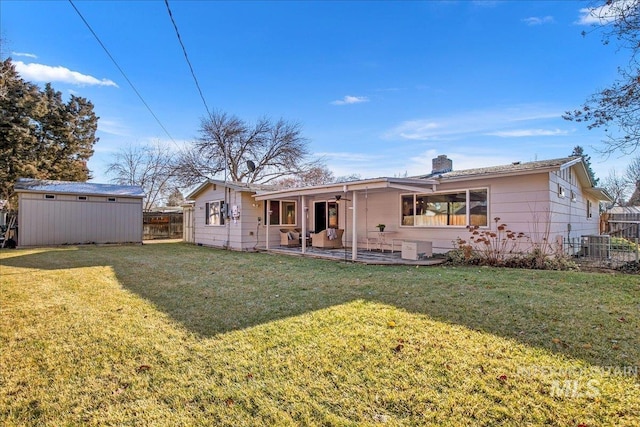 rear view of property featuring a patio area, a yard, and a storage unit