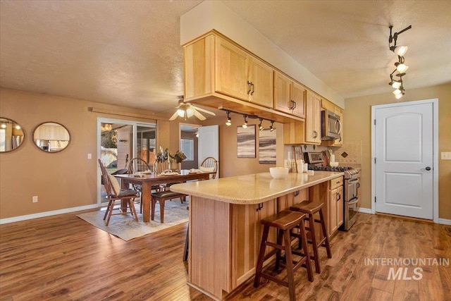 kitchen featuring a kitchen bar, ceiling fan, light brown cabinetry, appliances with stainless steel finishes, and dark hardwood / wood-style flooring