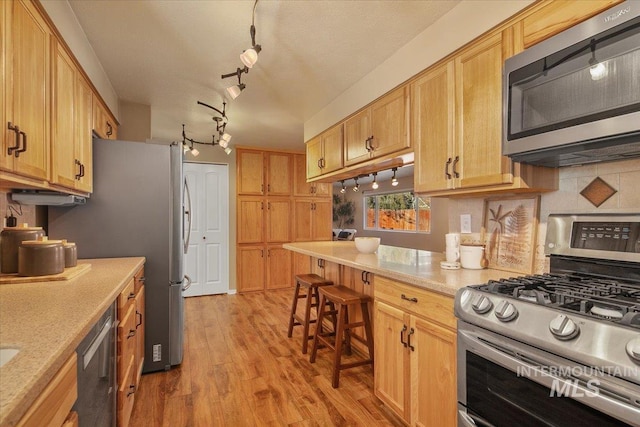 kitchen with track lighting, a breakfast bar area, light brown cabinetry, light hardwood / wood-style floors, and stainless steel appliances