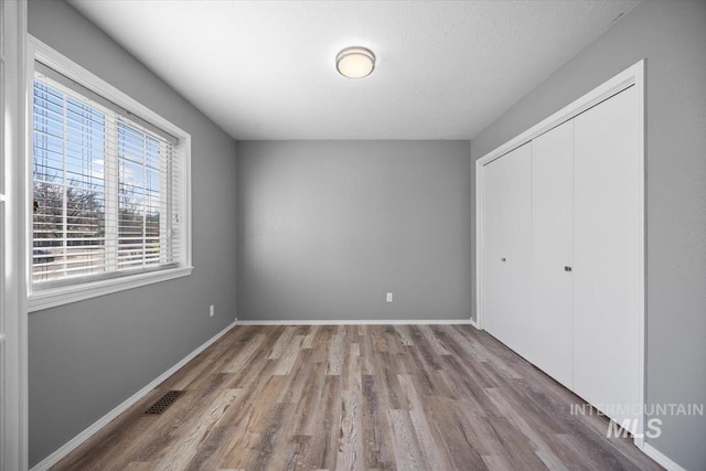 unfurnished bedroom with a closet, wood finished floors, baseboards, and visible vents