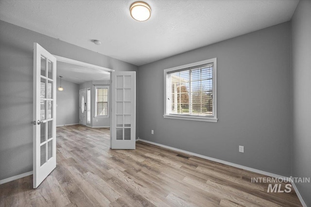 empty room with baseboards, french doors, a textured ceiling, visible vents, and wood finished floors