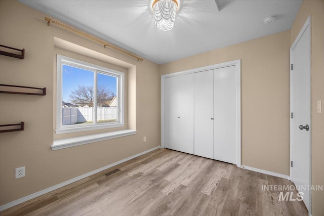 unfurnished bedroom with visible vents, a closet, baseboards, and wood finished floors