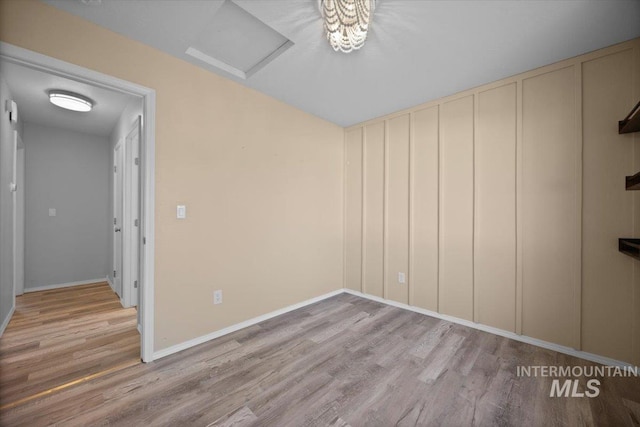 empty room featuring wood finished floors, attic access, and baseboards