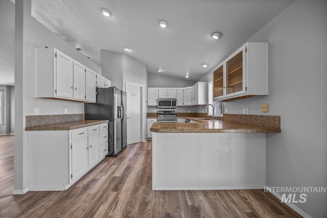 kitchen with white cabinets, appliances with stainless steel finishes, a peninsula, dark wood finished floors, and lofted ceiling