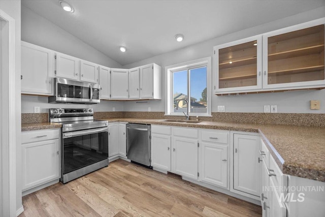 kitchen featuring vaulted ceiling, white cabinetry, light wood-style floors, stainless steel appliances, and a sink