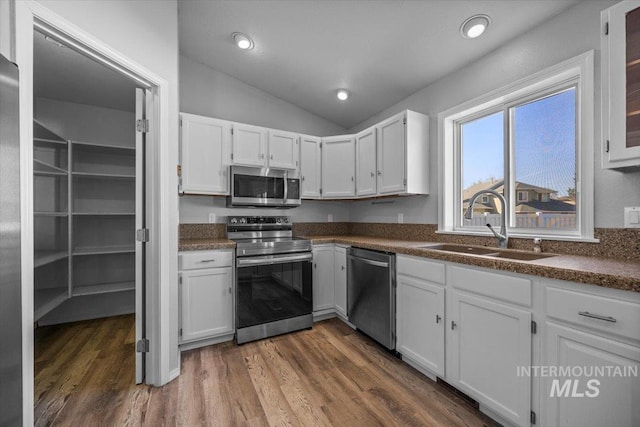 kitchen featuring a sink, appliances with stainless steel finishes, dark countertops, and white cabinetry
