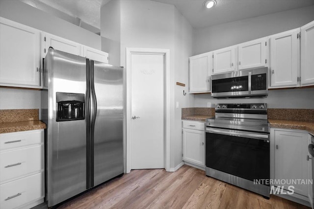 kitchen featuring appliances with stainless steel finishes, light wood finished floors, dark countertops, and white cabinets