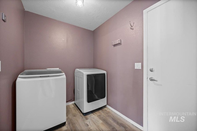 washroom with laundry area, a textured ceiling, wood finished floors, baseboards, and washer and clothes dryer
