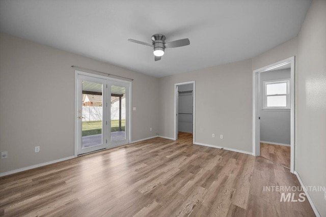 unfurnished bedroom featuring access to exterior, baseboards, multiple windows, and wood finished floors