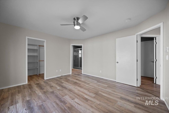unfurnished bedroom with a closet, baseboards, a spacious closet, a ceiling fan, and wood finished floors