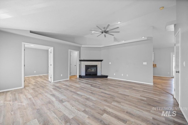 unfurnished living room featuring baseboards, ceiling fan, a tray ceiling, wood finished floors, and a glass covered fireplace