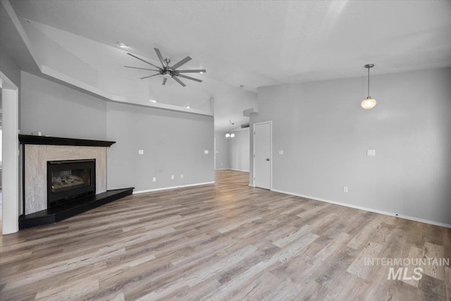 unfurnished living room featuring a fireplace with raised hearth, baseboards, a ceiling fan, and wood finished floors