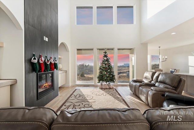 living room with an inviting chandelier, a fireplace, a high ceiling, and light hardwood / wood-style flooring