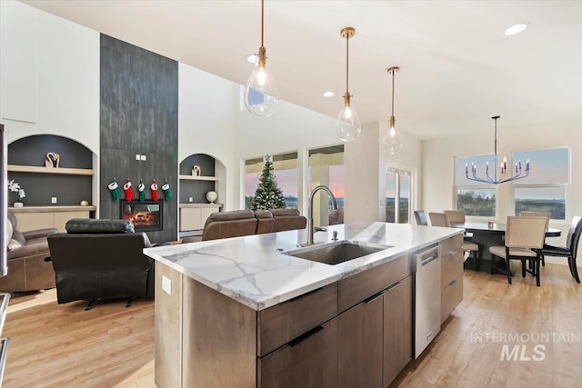 kitchen featuring sink, light hardwood / wood-style flooring, a notable chandelier, an island with sink, and a fireplace