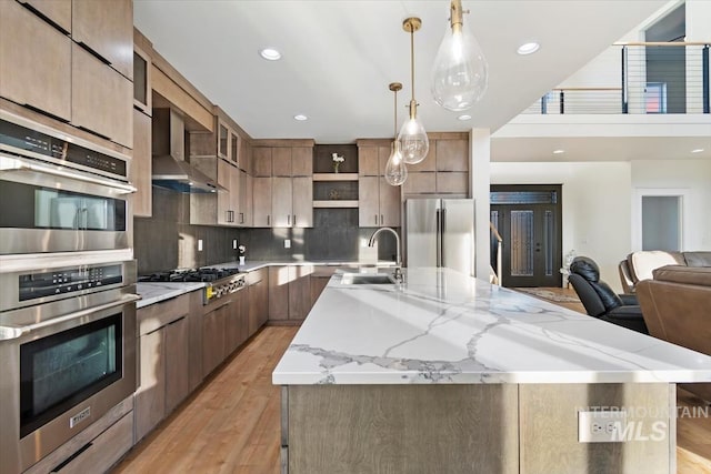 kitchen with a large island with sink, sink, light wood-type flooring, decorative light fixtures, and stainless steel appliances