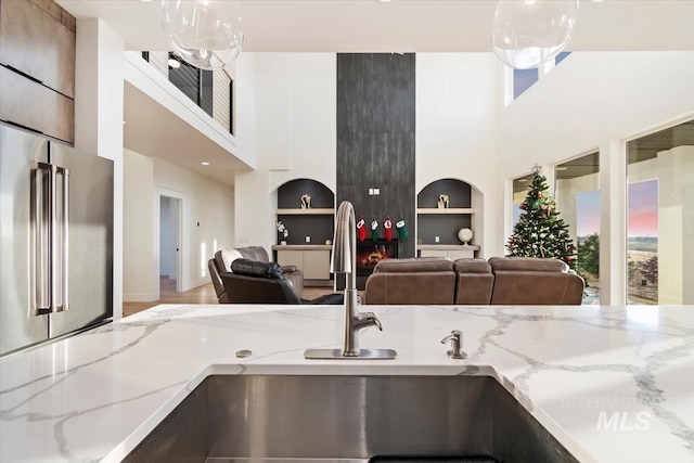kitchen featuring hardwood / wood-style floors, high end refrigerator, built in shelves, light stone countertops, and a towering ceiling