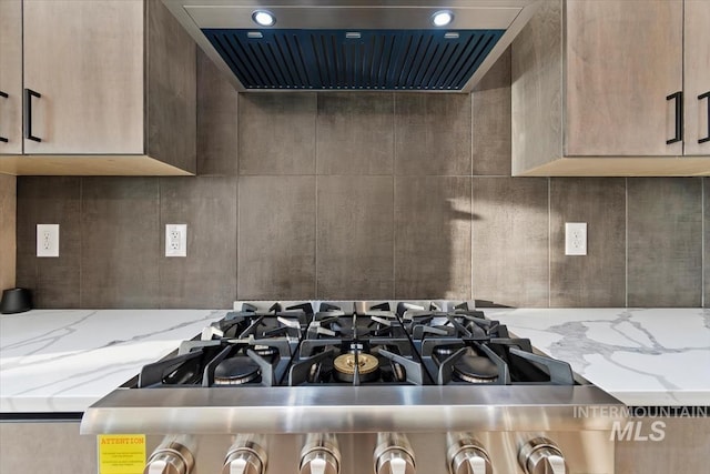 kitchen with light stone counters, wall chimney range hood, and range