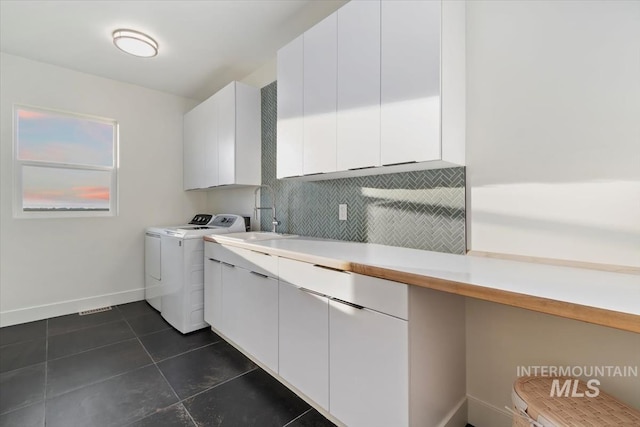 clothes washing area with dark tile patterned flooring, cabinets, independent washer and dryer, and sink