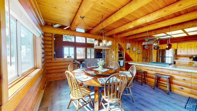 dining area featuring beam ceiling, a healthy amount of sunlight, rustic walls, and wood finished floors