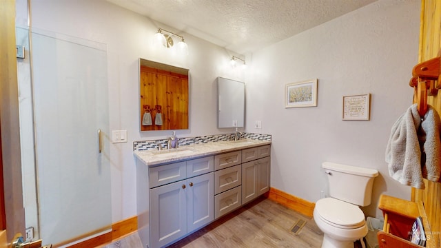 full bathroom featuring toilet, double vanity, wood finished floors, a textured ceiling, and a sink