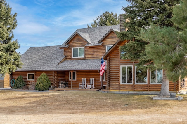 cabin with log exterior, a chimney, and a shingled roof