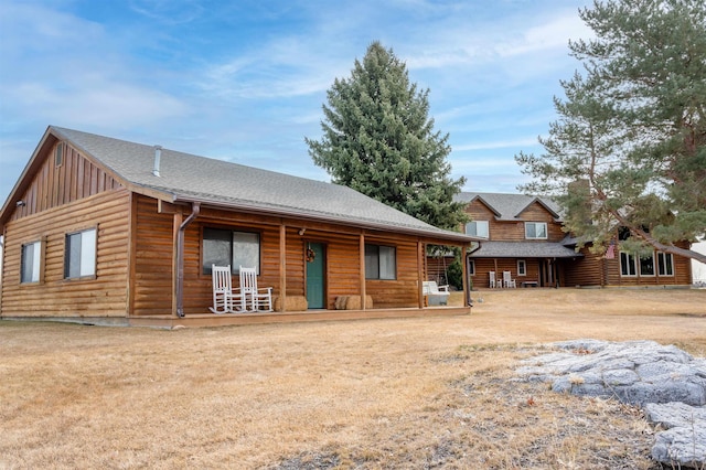 rear view of property with a yard, covered porch, and roof with shingles