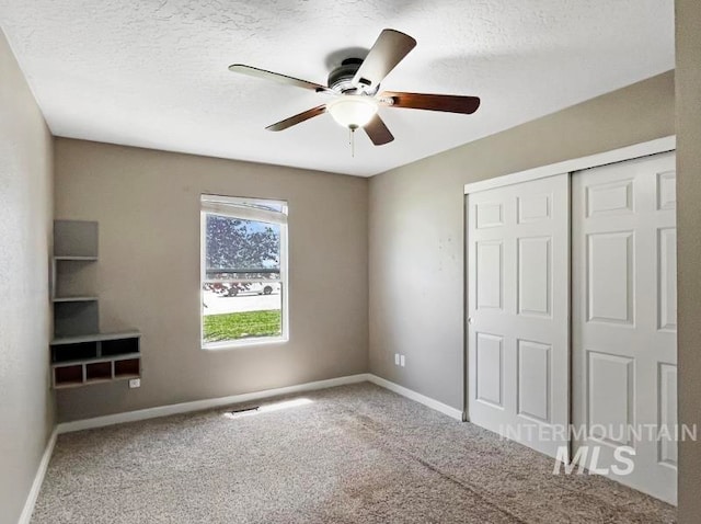 unfurnished bedroom with ceiling fan, a closet, a textured ceiling, and carpet flooring